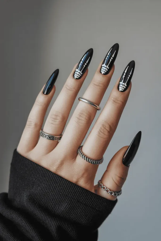 Black nails with delicate white skeleton hand outlines. Glossy finish, styled with silver rings for gothic aesthetic.