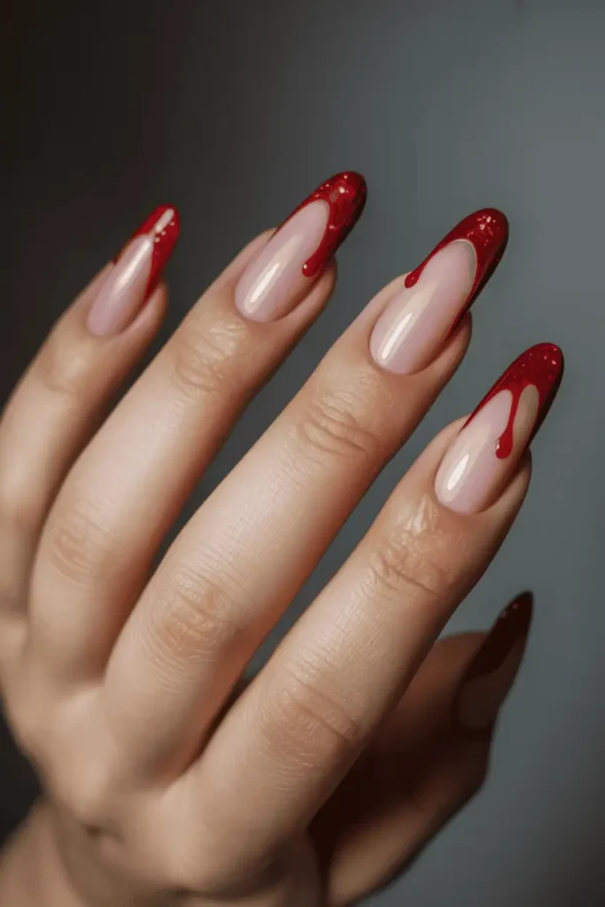 Nude nails with glossy red glitter drips starting from the cuticle. High-shine finish, styled against dark background for drama.