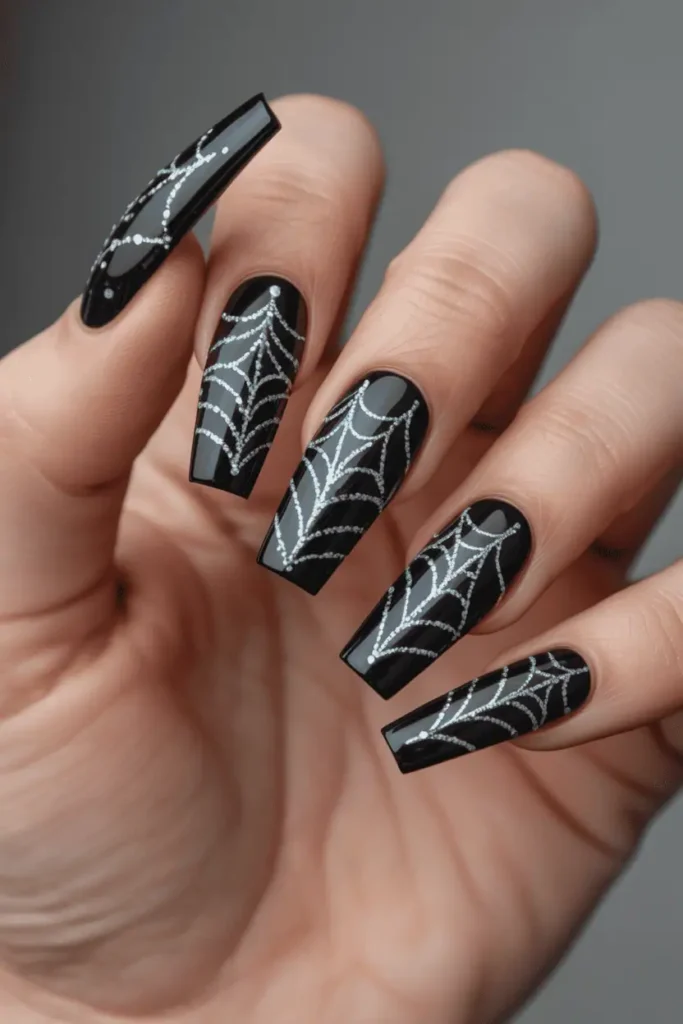 Long coffin nails with black base and delicate spiderweb patterns drawn in silver glitter. Party-style lighting, subtle sparkle effect.