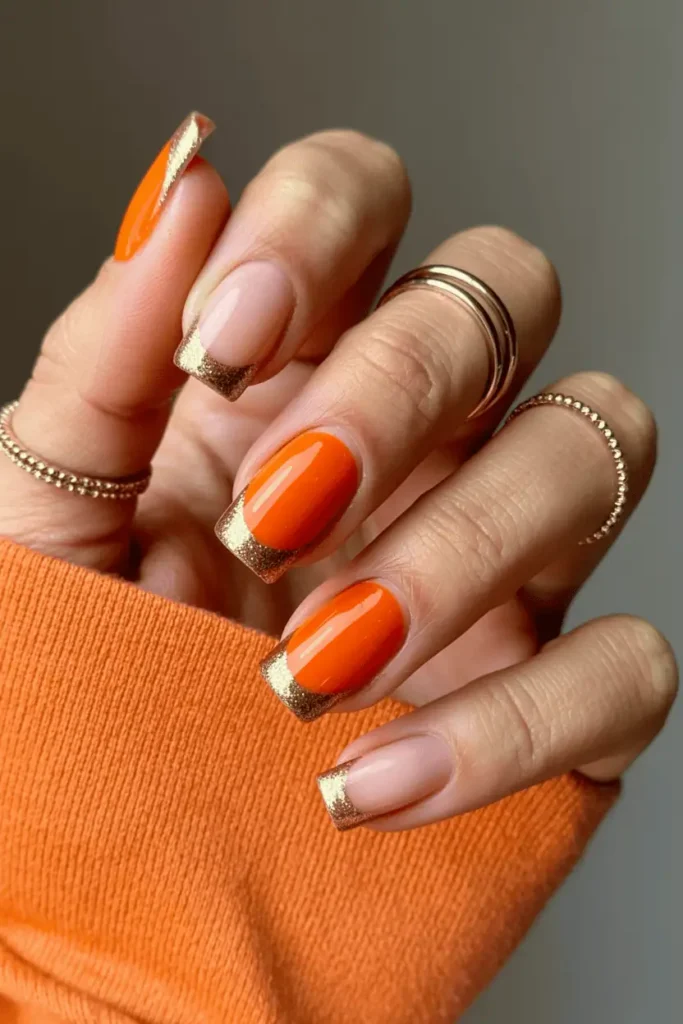 Pumpkin-orange nails with glittery gold French tips.