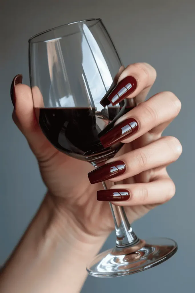 Glossy deep burgundy coffin nails holding a wine glass.