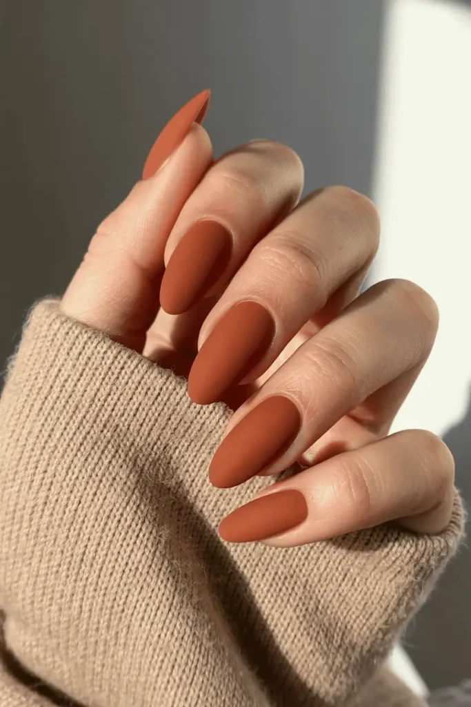 Burnt orange matte almond nails on cozy sweater background.