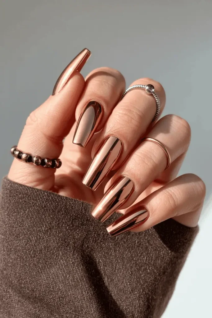 Metallic copper chrome coffin nails reflecting light, styled with earthy-toned accessories.