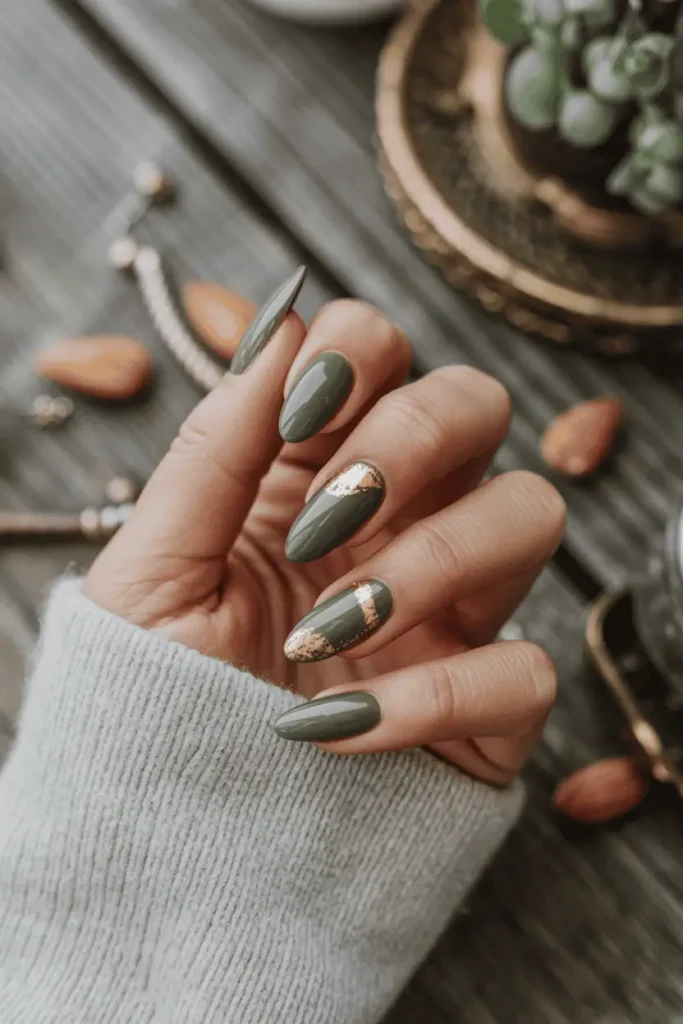 Olive green almond nails with delicate gold foil accents, rustic wooden table background.