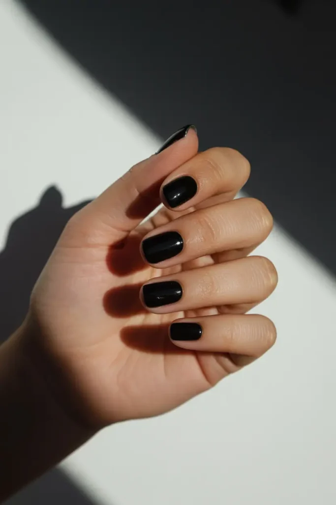 Short square nails with glossy black polish. Minimal studio background with white and black contrast.