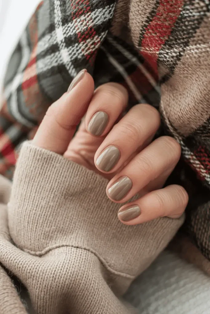Short rounded taupe nails styled with a plaid scarf and beige sweater.